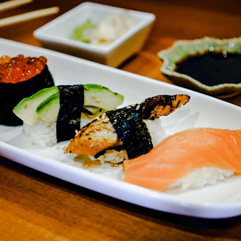 A white plate of Kenzo Thai & Sushi's nigiri and gunkan sushi with soy sauce and ginger.