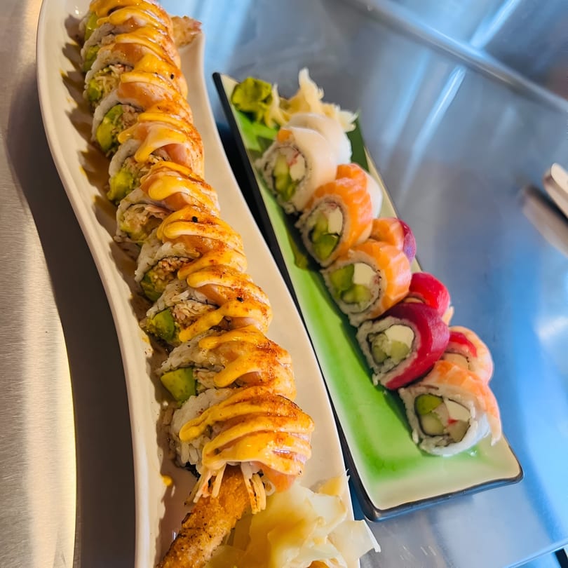 Two platters of colorful sushi rolls, one with orange sauce and the other with various toppings.