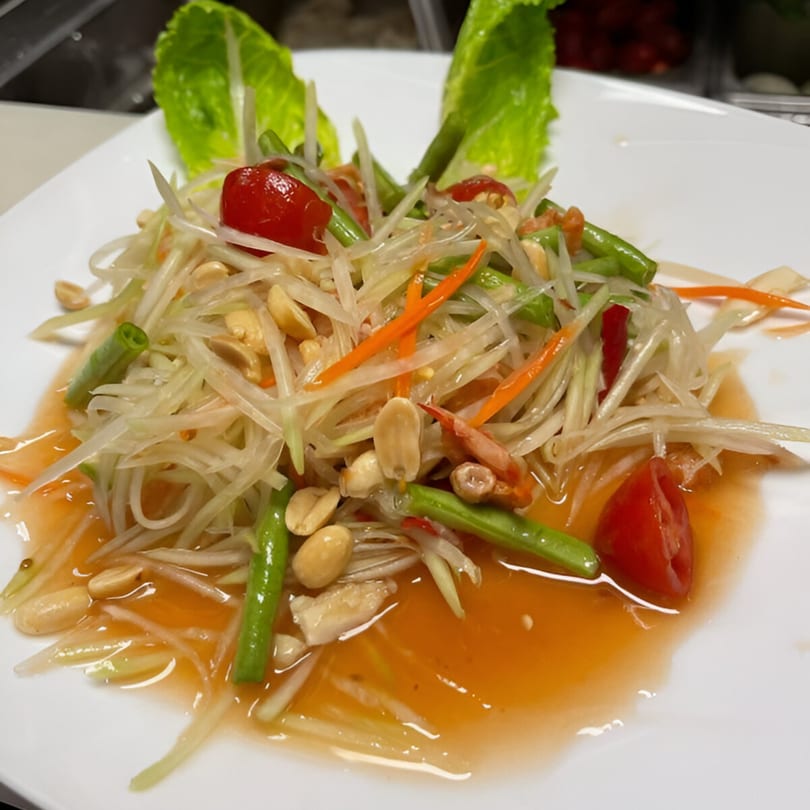Som Tum (papaya salad) with shredded papaya, green beans, peanuts, and cherry tomatoes in sauce.