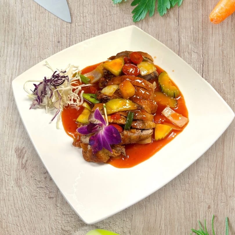 Sweet and sour duck with pineapple, bell peppers, and tomatoes, garnished with a purple orchid.