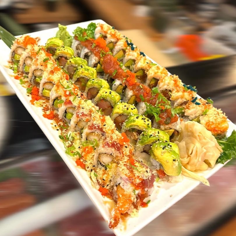 A long white platter filled with various colorful sushi rolls, garnished with sauces and toppings.
