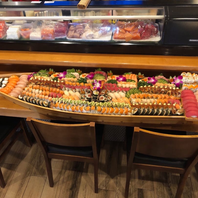 A large wooden boat filled with various sushi rolls and sashimi, with a sushi bar in the background.