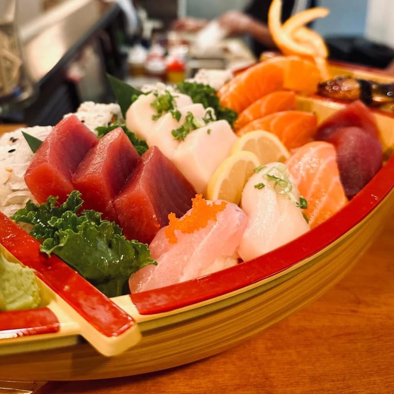A sushi boat filled with various sashimi, including tuna, salmon, and white fish, garnished with lemon and greens.