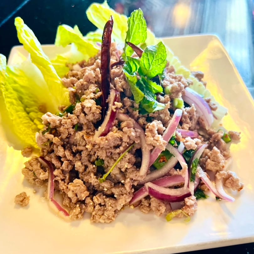 Minced meat salad with red onions, mint, and chili, served with fresh lettuce on a white plate.