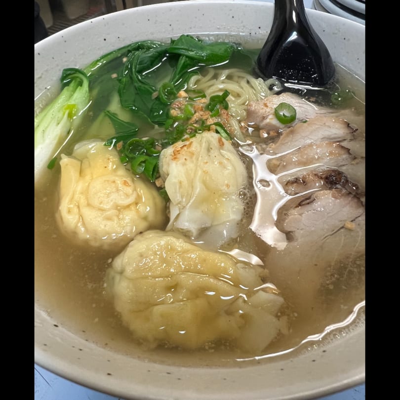 A bowl of Kenzo Thai & Sushi ramen with pork, wontons, noodles, and green vegetables.