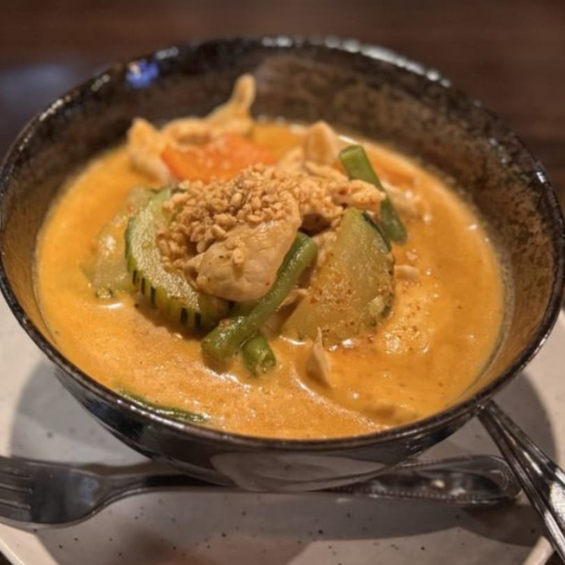A bowl of Kenzo Thai & Sushi's red curry with chicken, green beans, and zucchini, topped with peanuts.