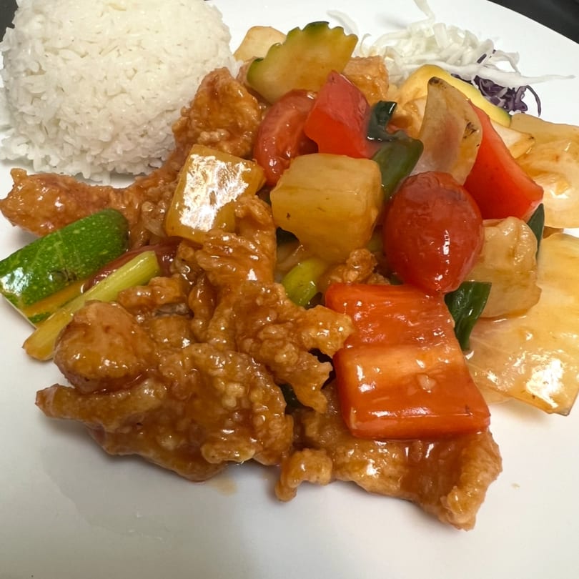 Sweet and sour chicken with bell peppers, pineapple, zucchini, and white rice on a plate.