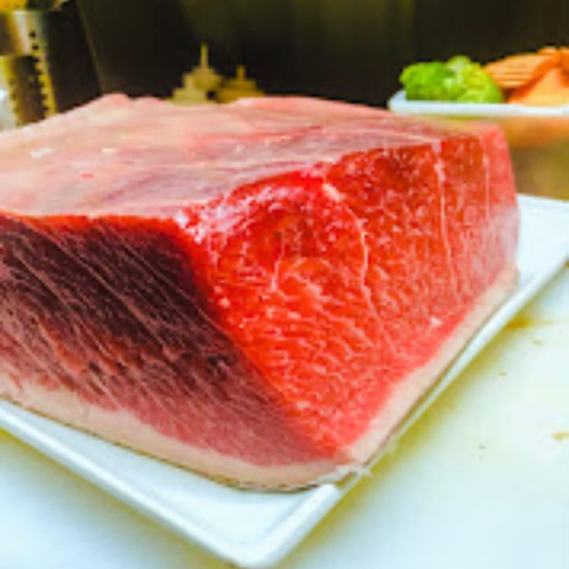 Large block of fresh red tuna on a white plate, with vegetables in the background.
