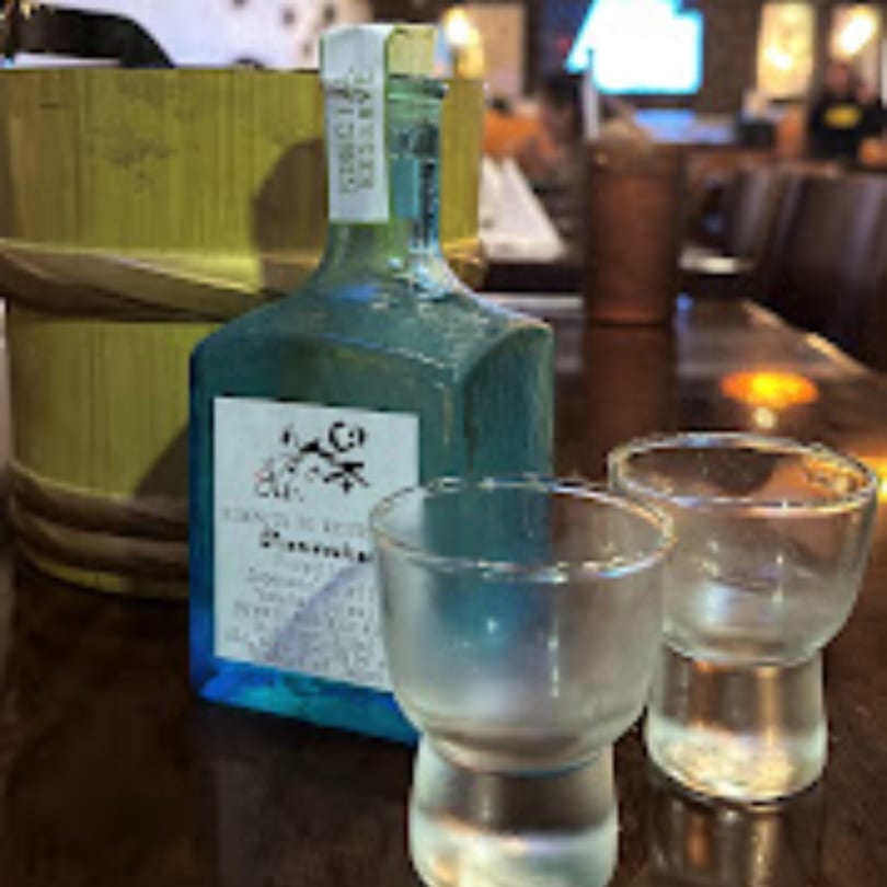 A blue bottle of sake and two small clear glasses on a dark wooden table.