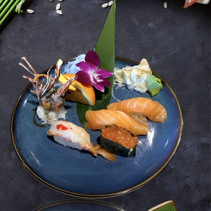 Assorted Kenzo Thai & Sushi nigiri and gunkan sushi with salmon, shrimp, and roe on a blue plate.