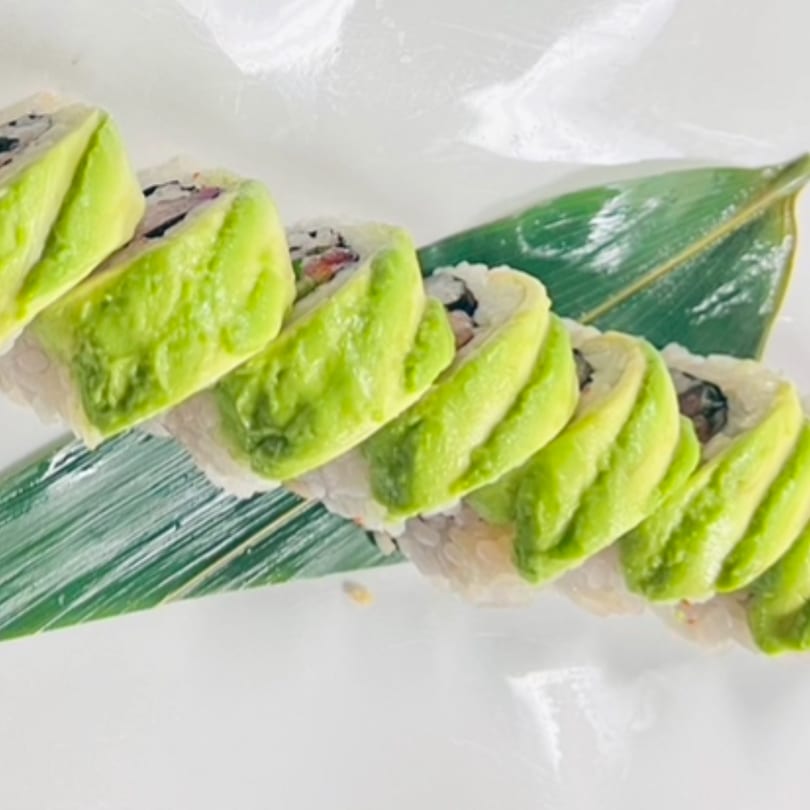 Kenzo Thai & Sushi's avocado-topped sushi roll, presented on a green leaf against a white background.