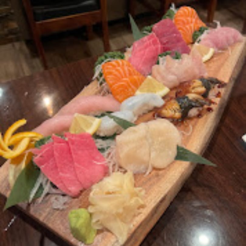 A large wooden platter of Kenzo Thai & Sushi sashimi and nigiri, garnished with lemon and ginger.