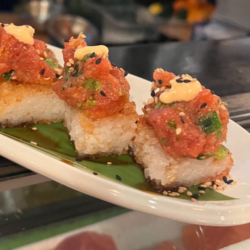 Three Kenzo Thai & Sushi crispy rice tuna bites with spicy mayo and sesame seeds on a white plate.