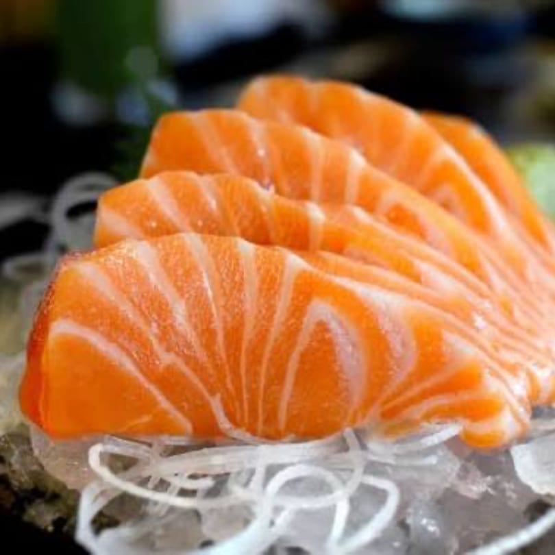 Close-up of vibrant orange salmon sashimi slices, artfully arranged on a bed of white shredded daikon.
