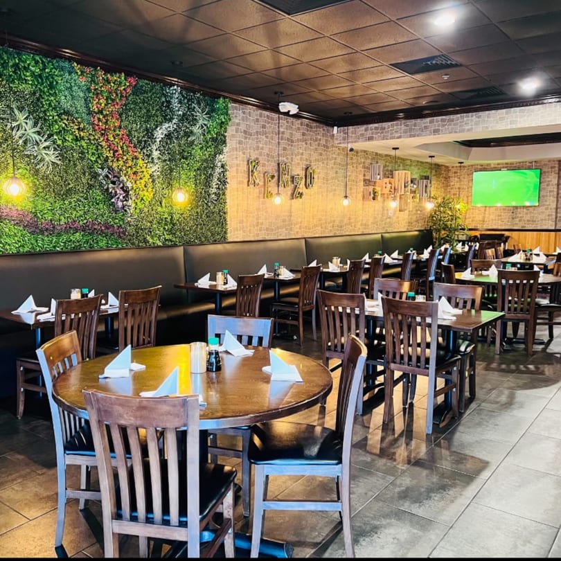Interior of Kenzo Thai & Sushi restaurant with tables, chairs, and a green plant wall.