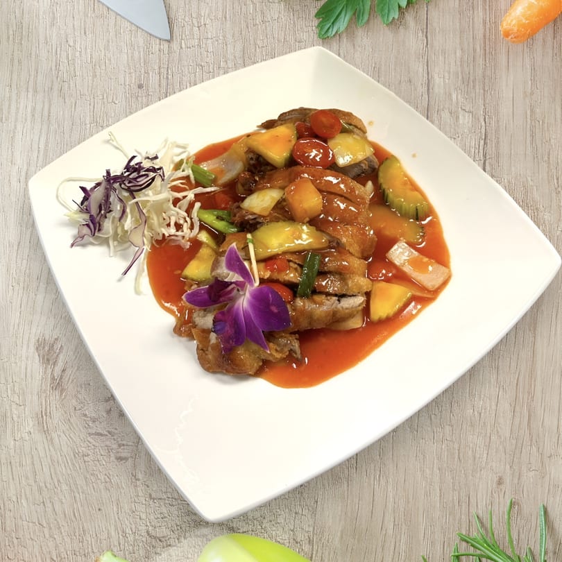 Crispy duck in sweet and sour sauce with pineapple, tomatoes, and a purple orchid garnish.