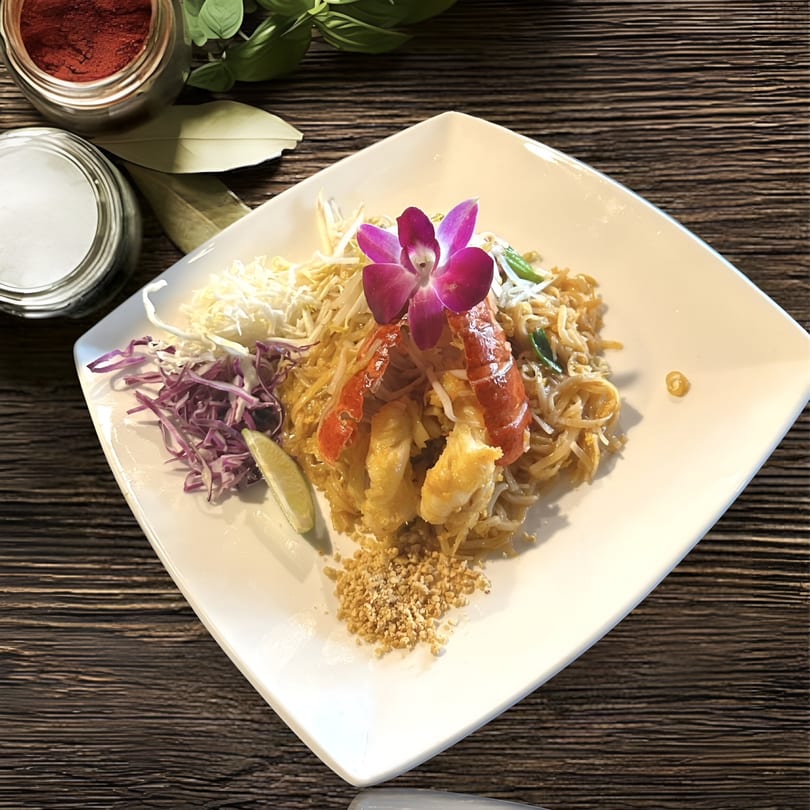 Kenzo Thai & Sushi's Pad Thai with lobster, garnished with a purple orchid, lime, and shredded cabbage.