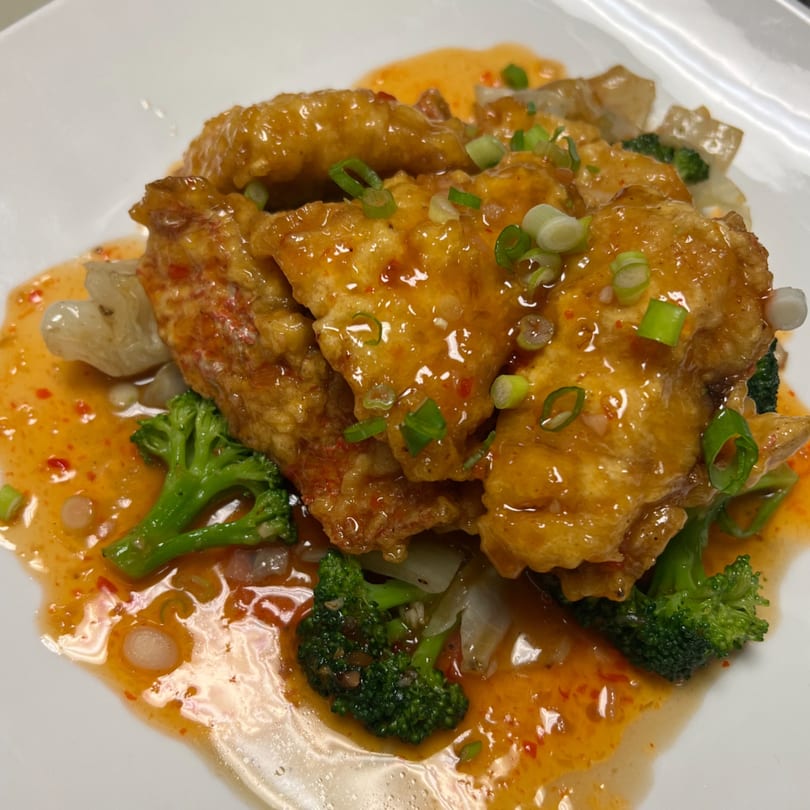 Crispy chicken or fish pieces coated in orange sauce, garnished with green onions and broccoli.