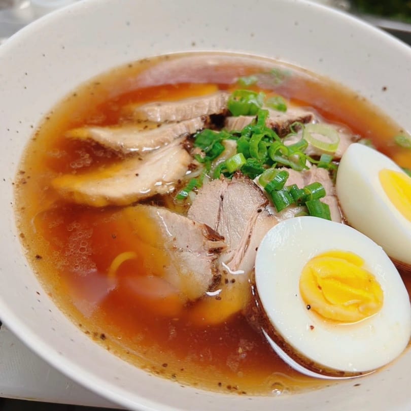 Close-up of a Kenzo Thai & Sushi ramen bowl with pork, green onions, and two hard-boiled egg halves.