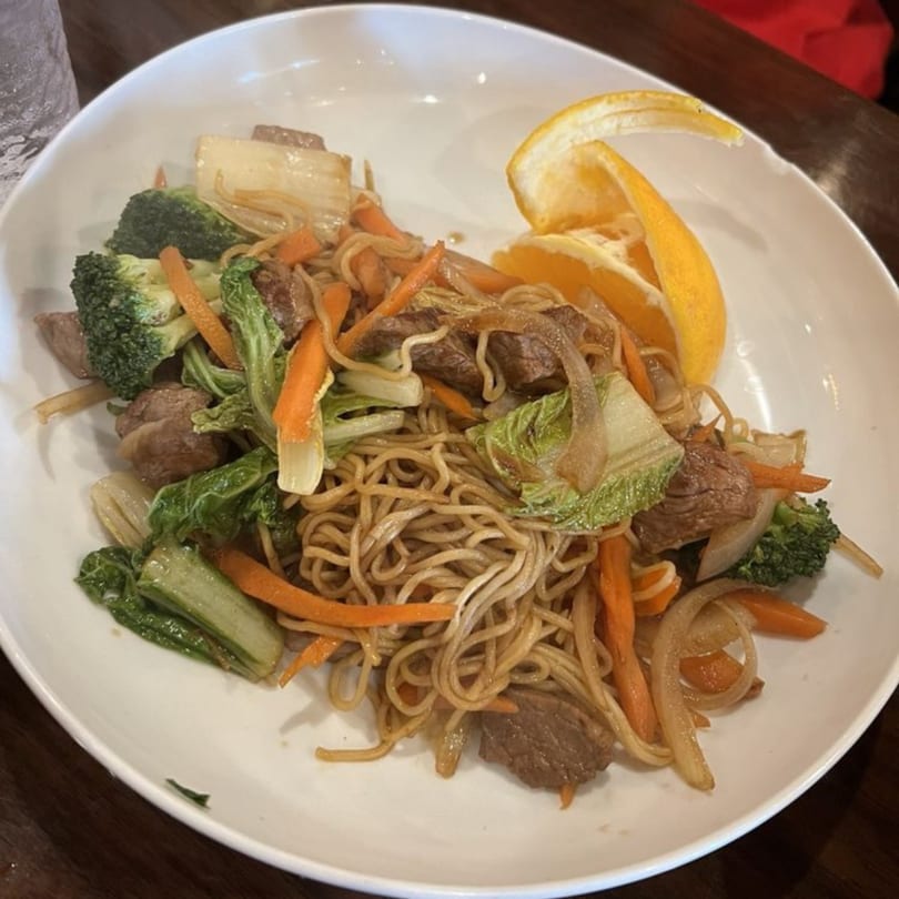 A white bowl filled with Kenzo Thai & Sushi's beef lo mein, broccoli, carrots, and orange slices.