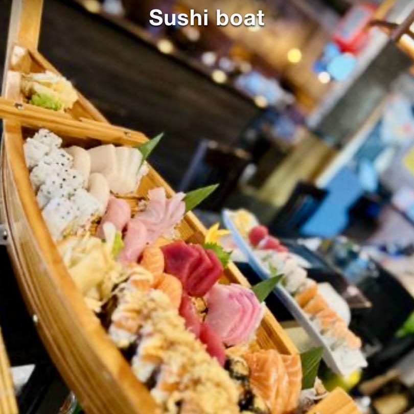 A wooden sushi boat filled with various sushi rolls, sashimi, and pickled ginger at Kenzo Thai & Sushi.